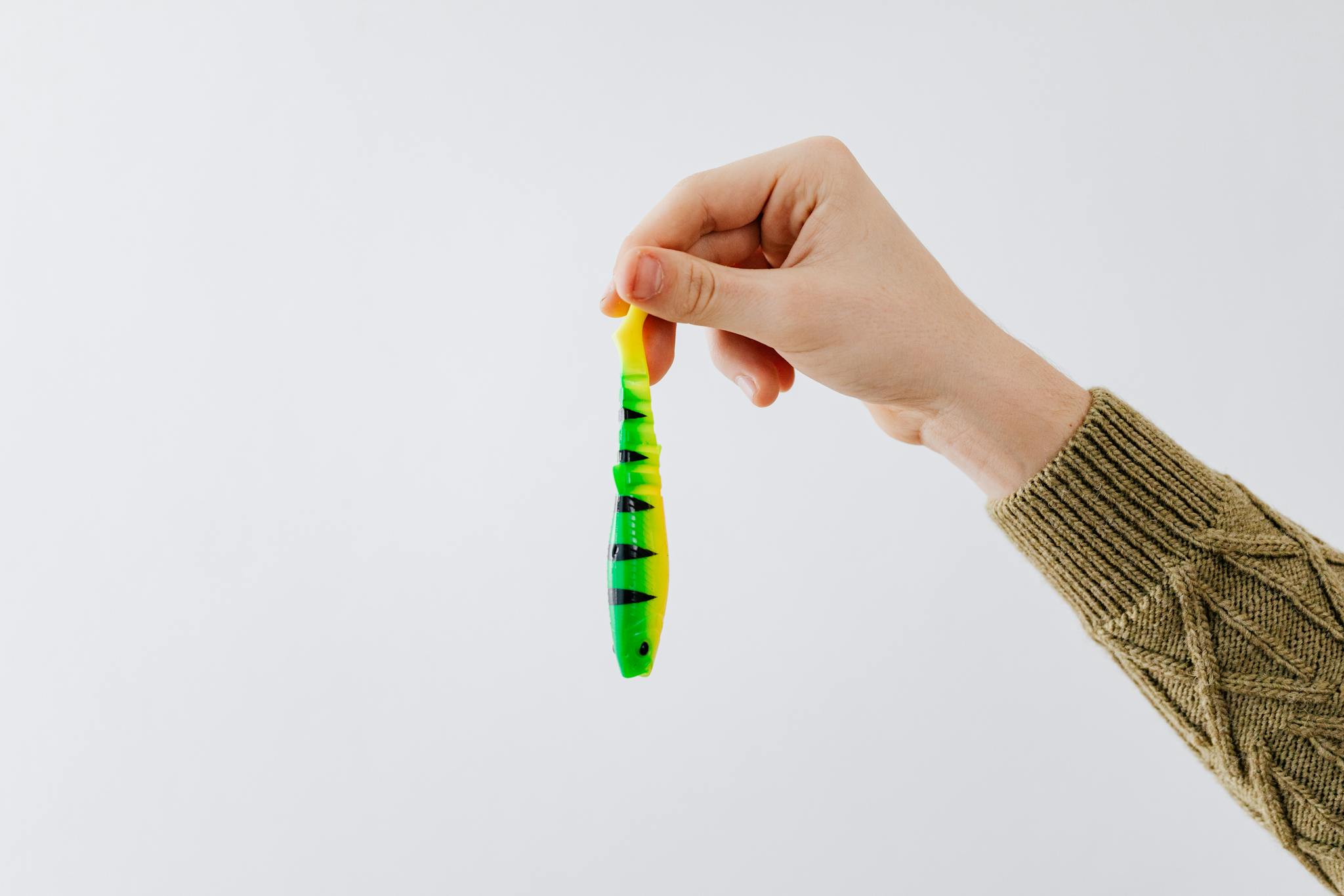 Close-up of a hand holding a vibrant fishing lure against a white background, ideal for fishing topics.