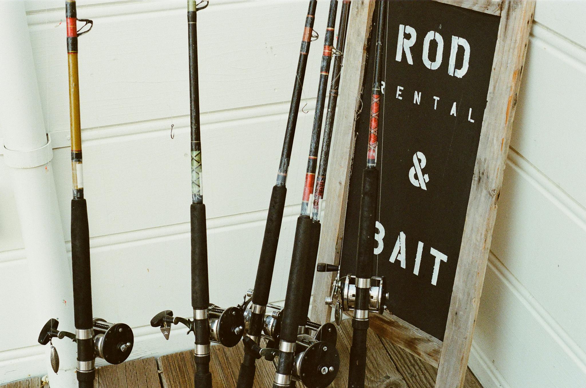 Collection of fishing rods beside a bait rental sign outdoors.