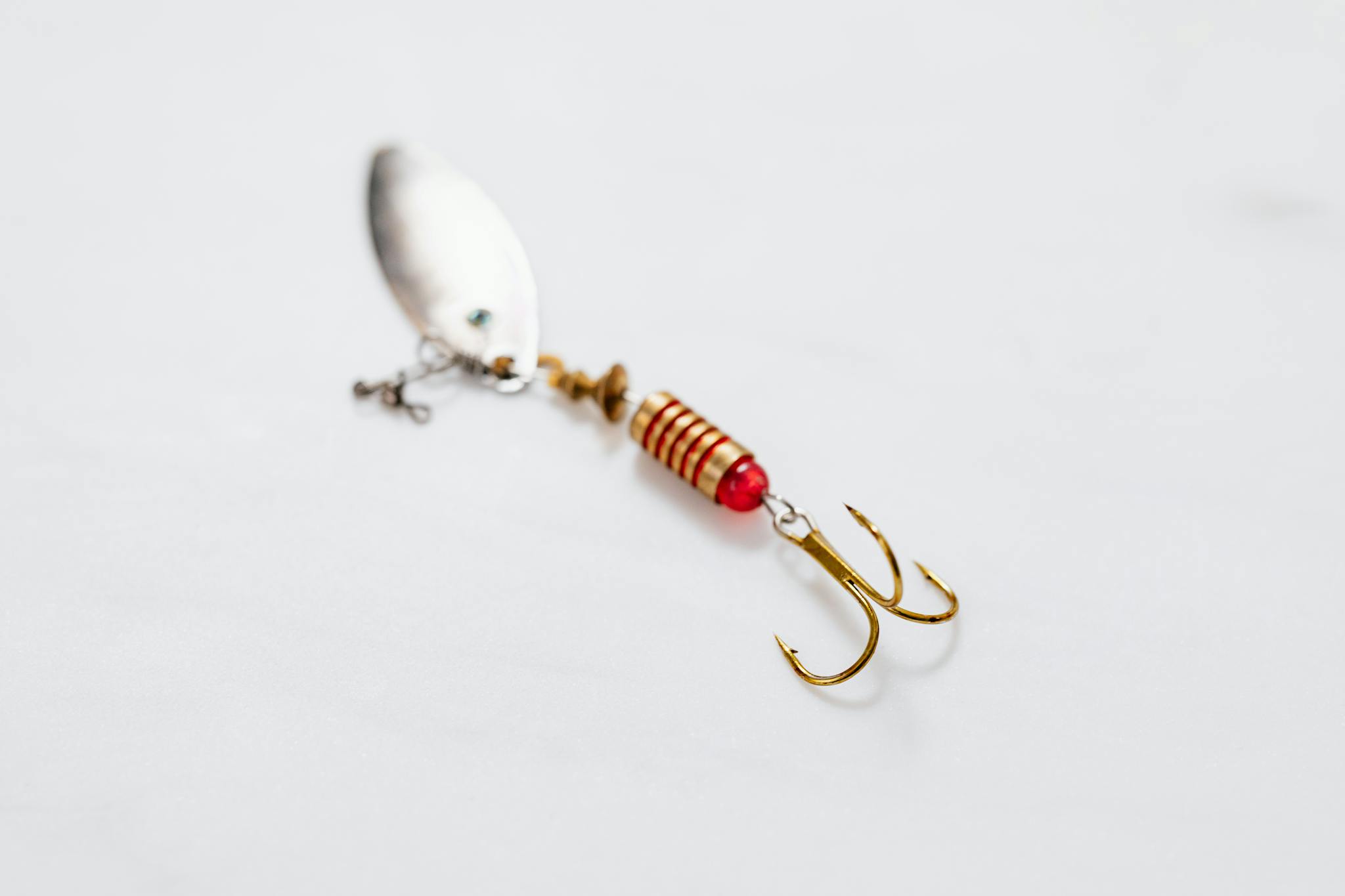Detailed view of a metallic fishing lure with a sharp treble hook on white surface.