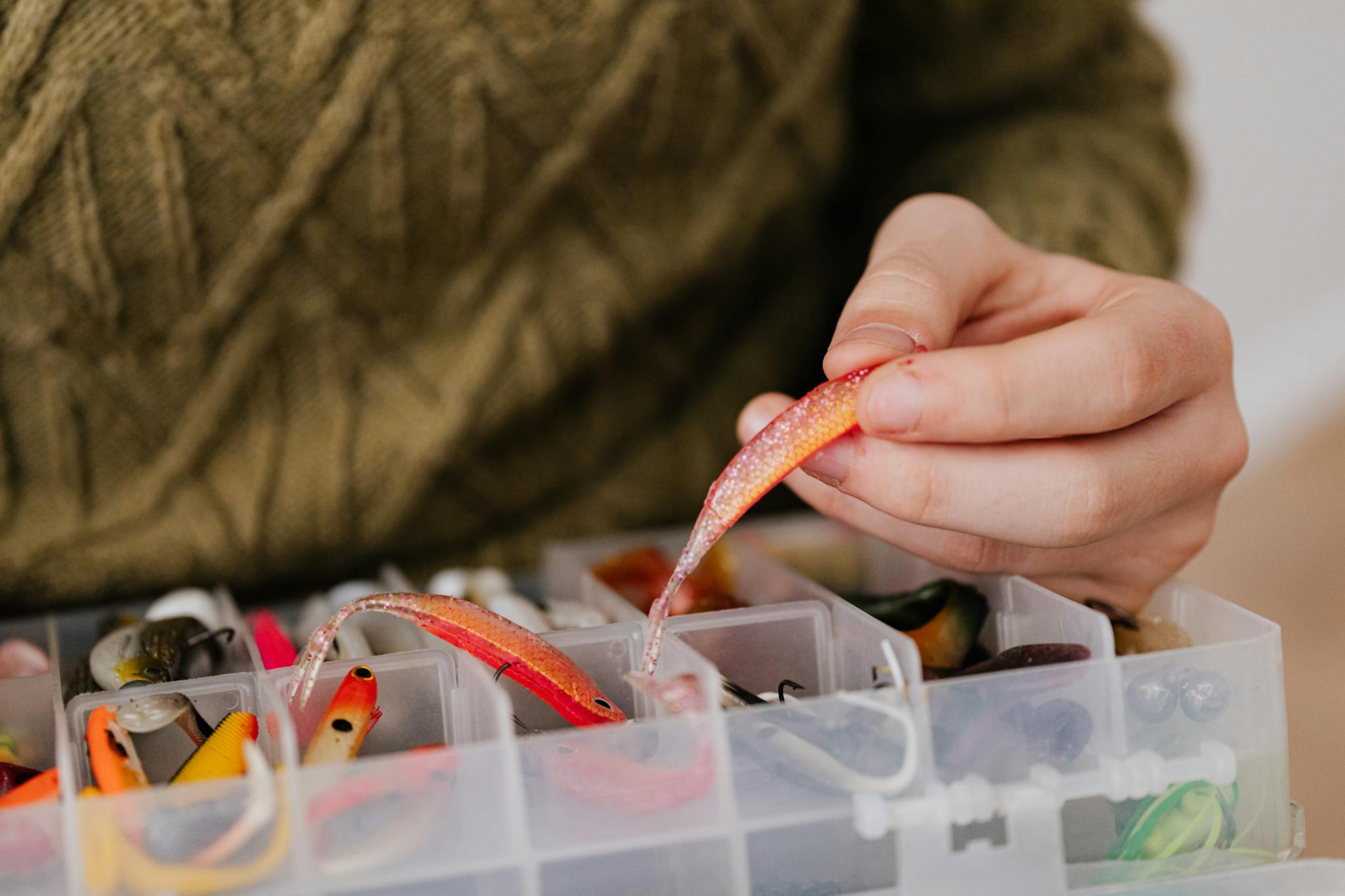 Hand selecting vibrant fishing lure from plastic container. Perfect for angling enthusiasts.